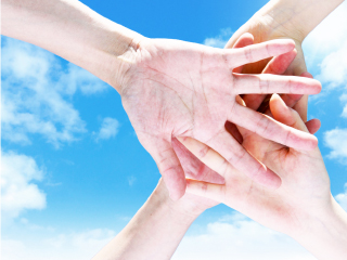 イメージ画像: 青空を背景に、4人が右手を上に重ねている